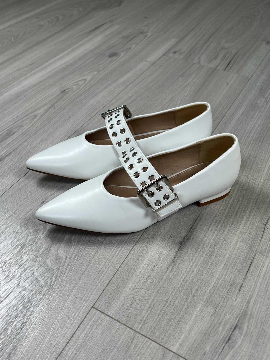 Ballerina a punta bianca con cinghietta regolabile e calzata regolare su pavimento in legno