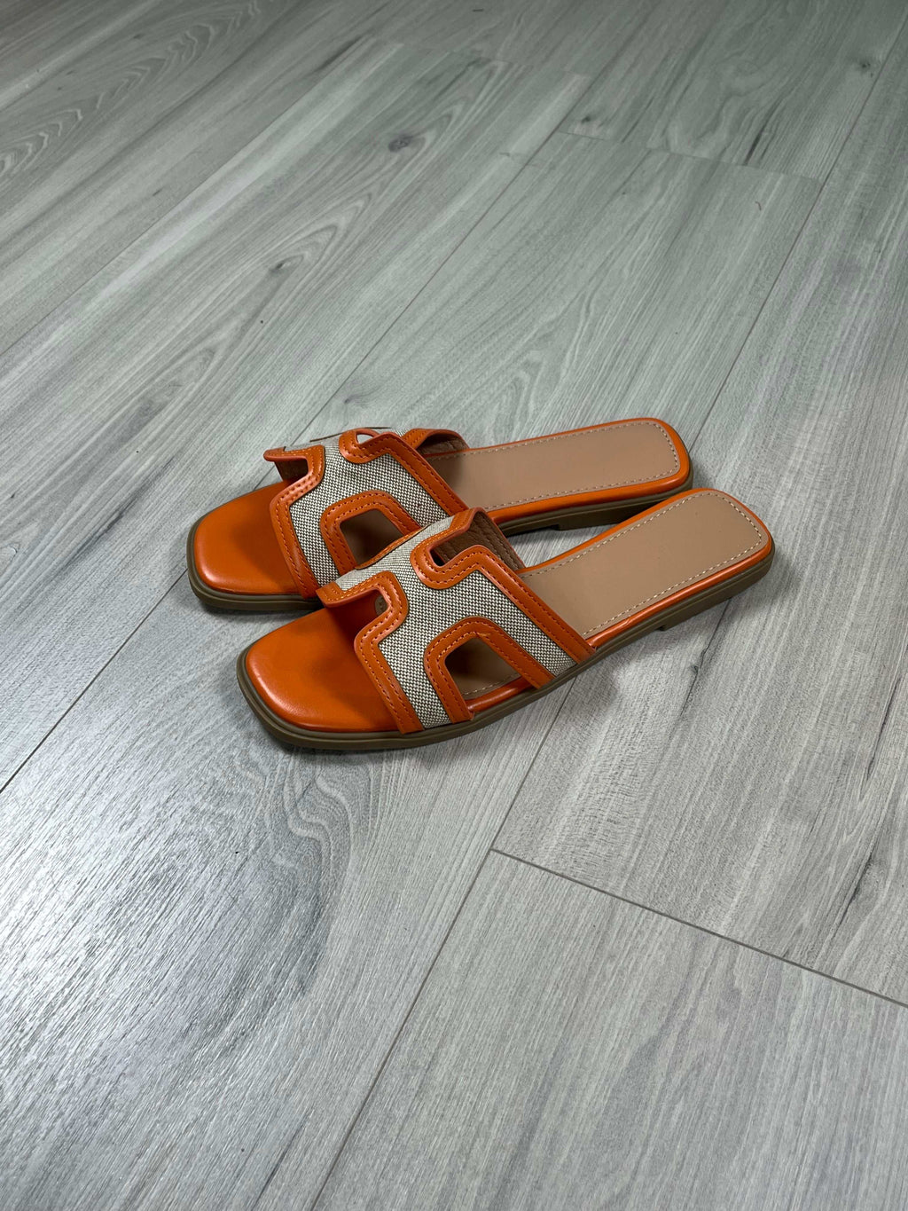 Ciabattina Kelly Arancio orange flat slide sandals with narrow sole on wooden floor