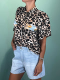 Woman wearing short sleeve Camicia Animalier with leopard print and Hawaii patch paired with light denim shorts