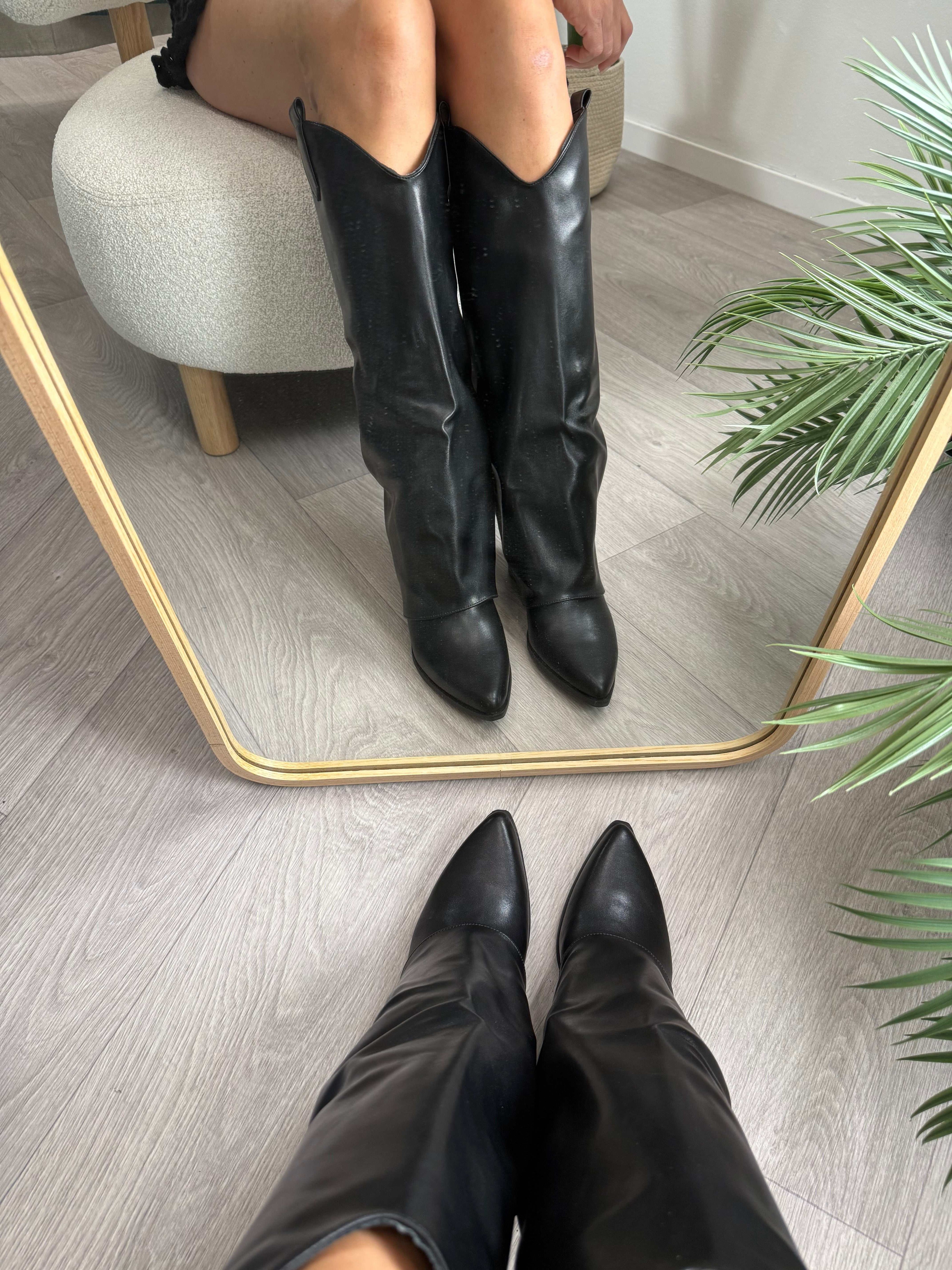 Black knee-high Stivale Nero boots with maxi cuff and 5cm heel on wooden floor with mirror reflection.