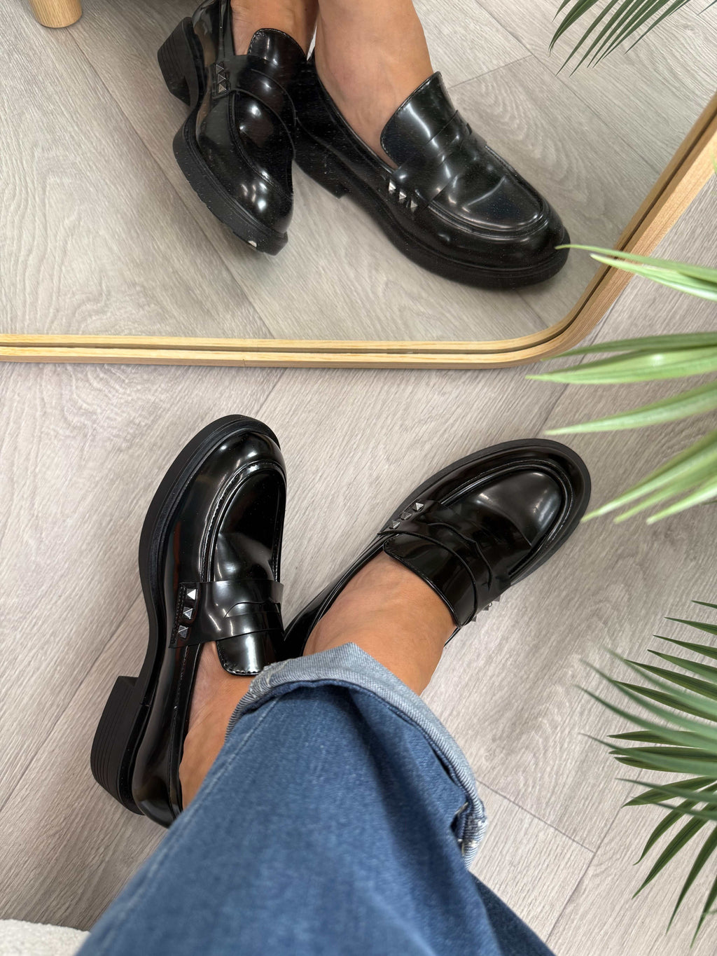 Mocassino lucido nero con borchiette laterali e vestibilità regolare su pavimento in legno chiaro