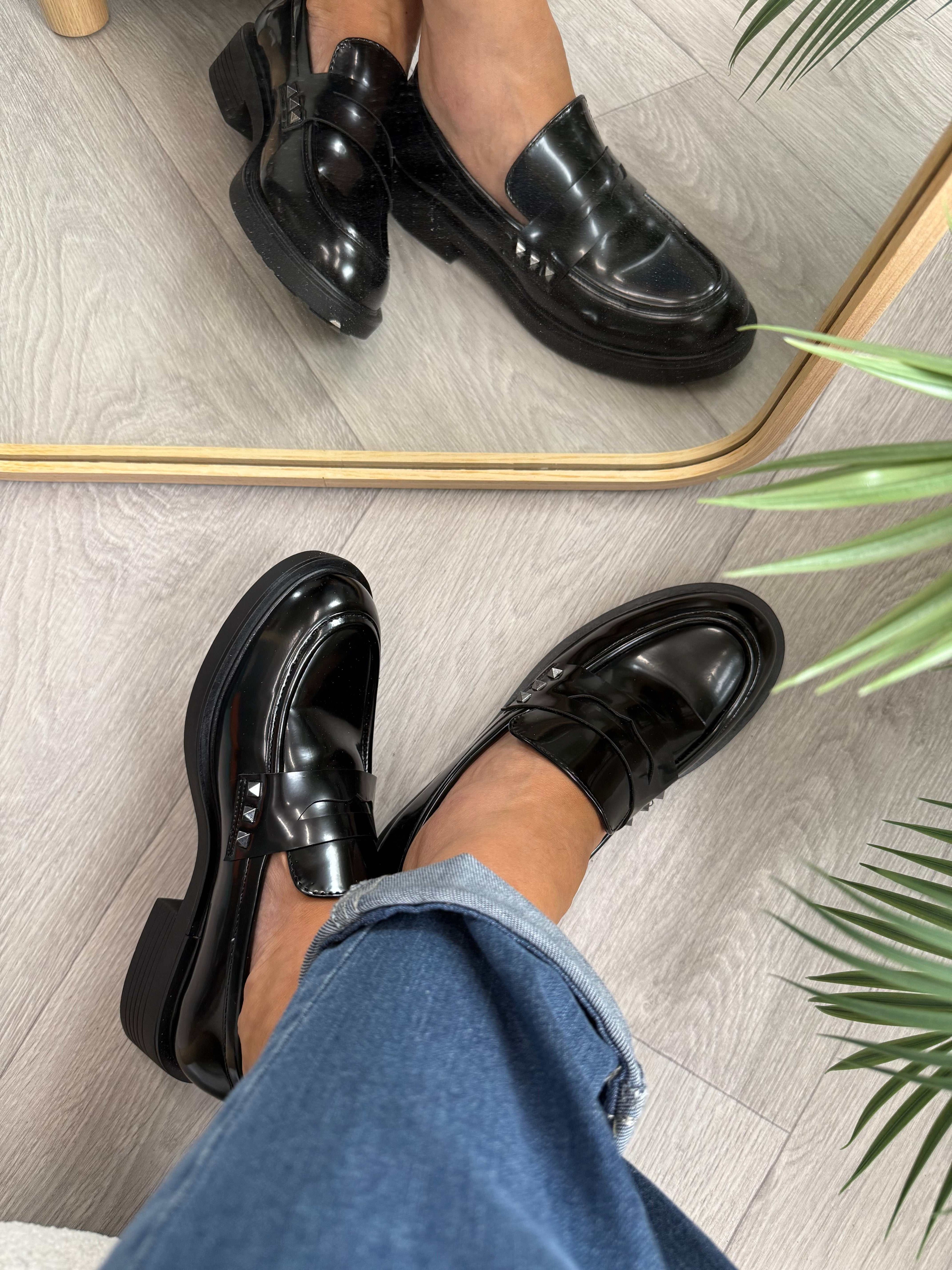 Mocassino lucido nero con borchiette laterali e vestibilità regolare su pavimento in legno chiaro