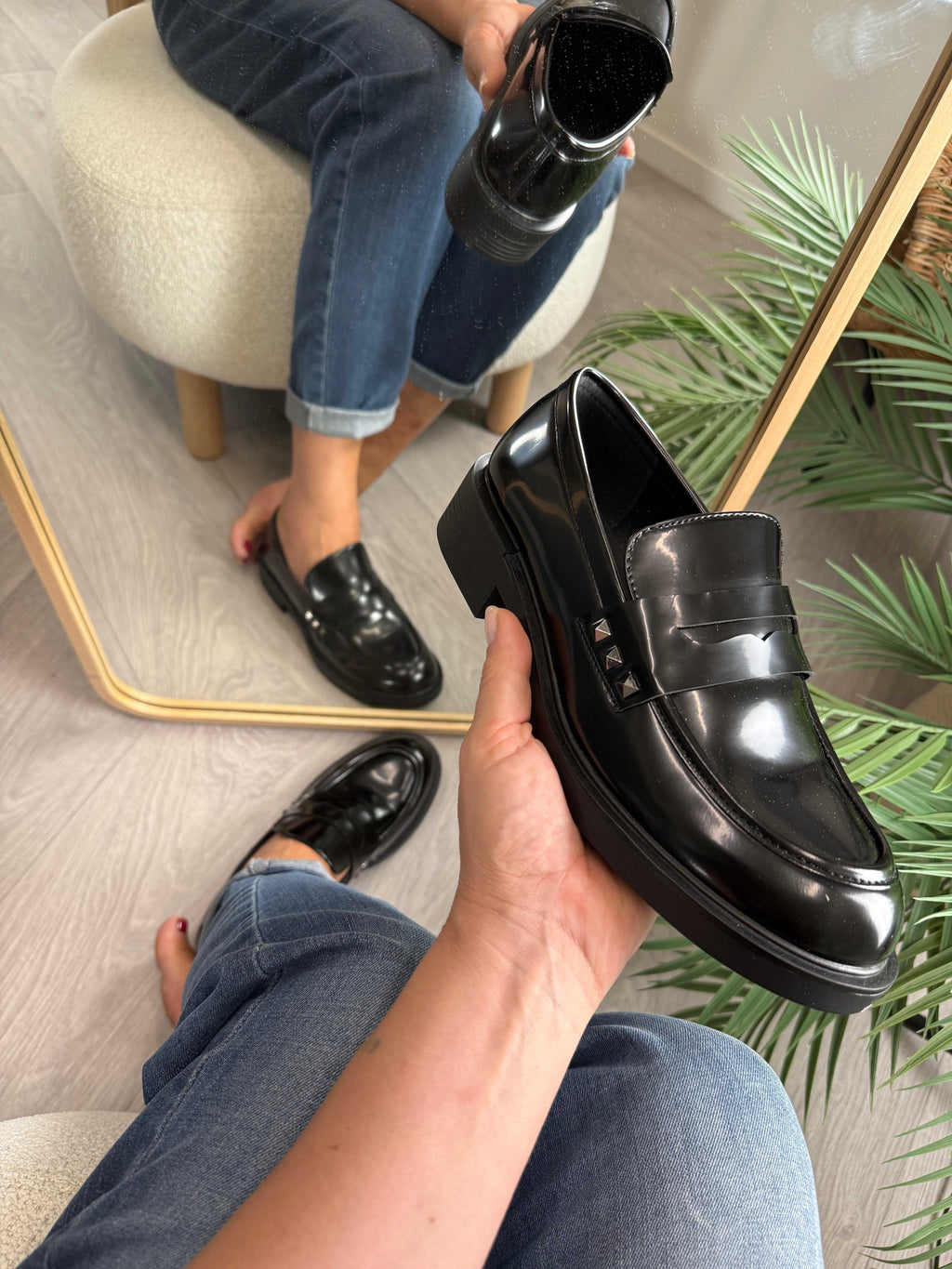 Mocassino lucido nero con borchiette laterali indossato e tenuto a mano davanti a uno specchio