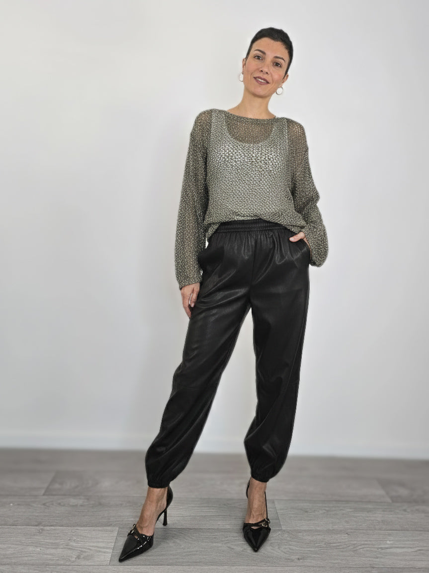 Modella indossa jogger neri in ecopelle con elastico in vita e alle caviglie, abbinati a maglia traforata grigia e tacchi a spillo neri.