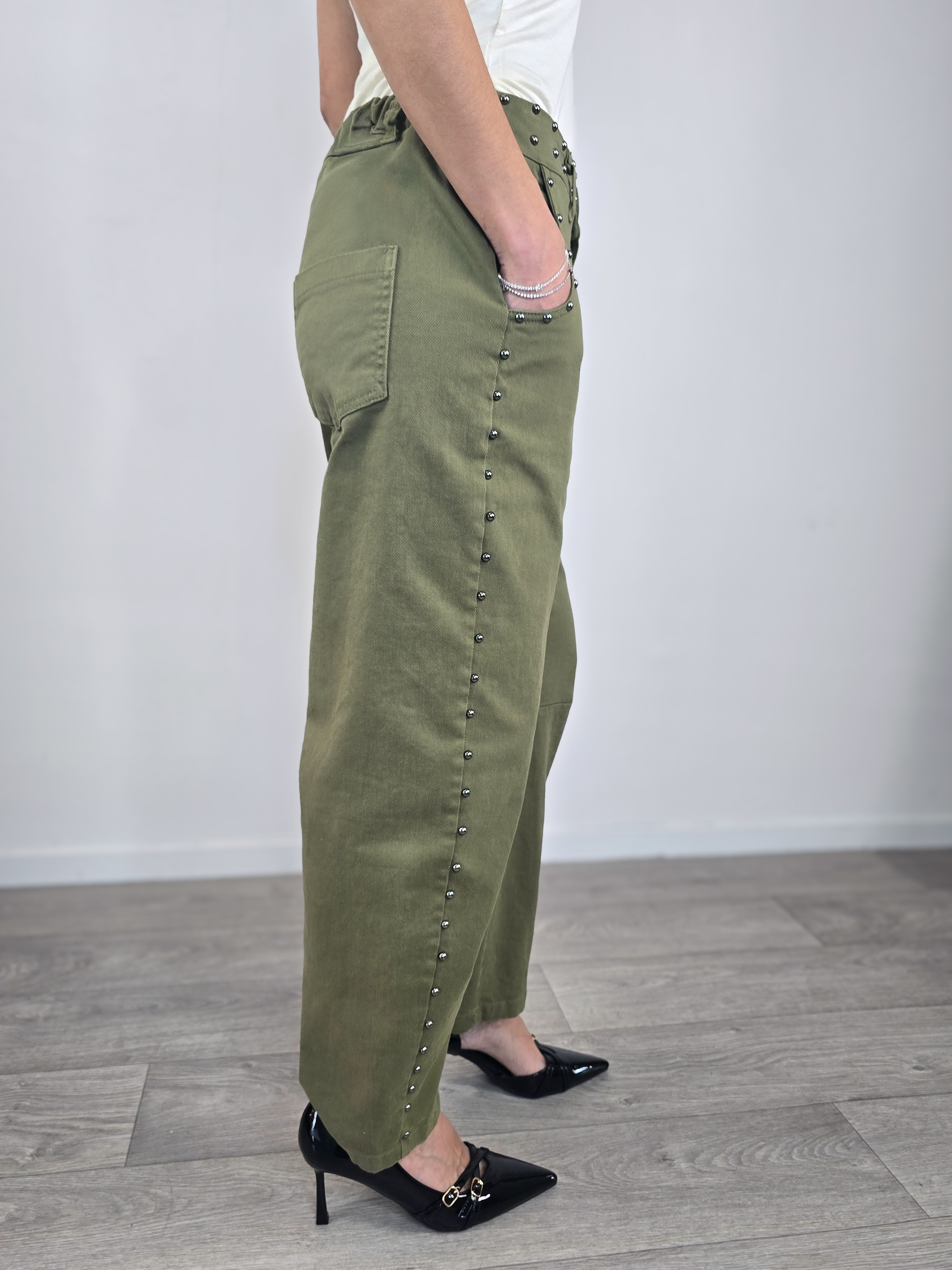 Pantaloni Kontatto in cotone verde militare dal taglio baloon, caratterizzati da profili con borchie metalliche e abbinati a scarpe décolleté nere.
